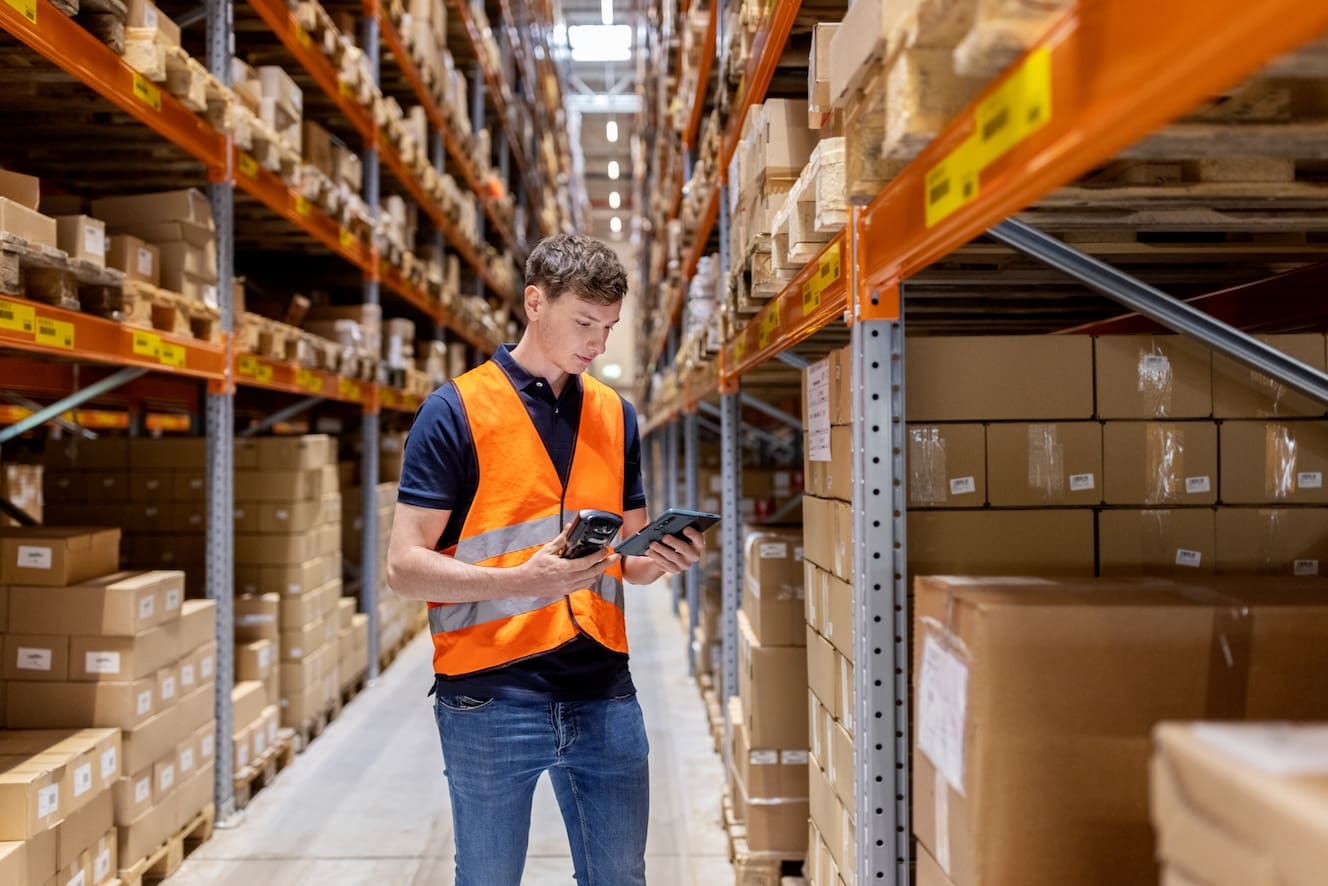 A young man in a warehouse holding a portable scanner.